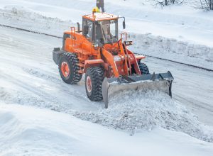 Big orange tractor cleans up snow from the road and loads it into the truck. Cleaning and cleaning of roads in the city from snow in winter